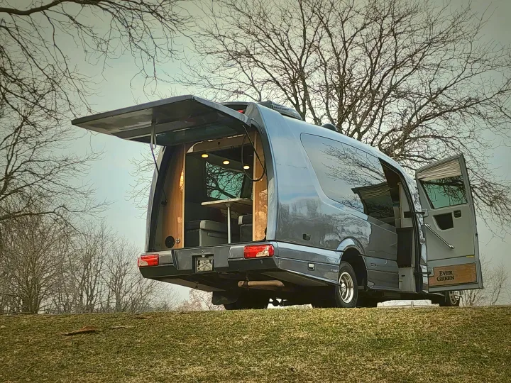 This gray custom camper van, perfect for rv rental, reveals its cozy, lit interior with open rear hatch & side door on a grassy hill.. Other Other 2016