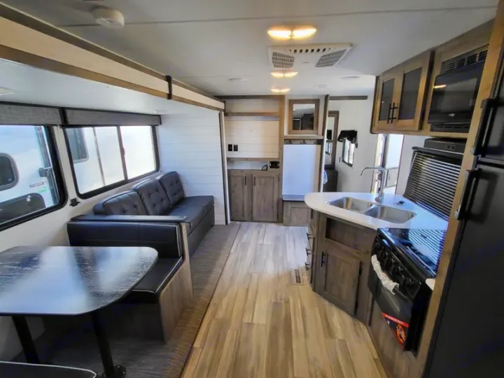 Bright, modern RV rental interior featuring a kitchen with sink/stove, and a living area with a comfy dinette and sofa.. Heartland Pioneer BH270 2023