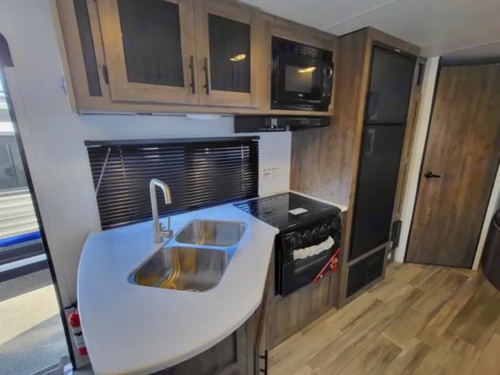 RV rental kitchen: Features a double sink, countertop, microwave, oven/stove, refrigerator, and wood-paneled cabinets.. Heartland Pioneer BH270 2023