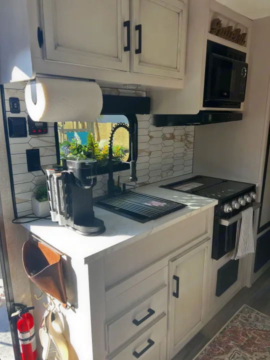 Bright, modern RV rental kitchen: white cabinets, hexagonal backsplash, stove, microwave, Keurig, & paper towel dispenser.. Jayco Featherlight SLX8 2022