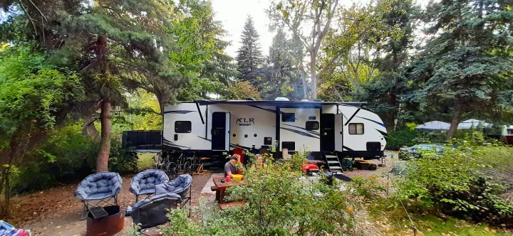Camping fun: An XLR Boost RV rental is set up in a wooded campsite with people at a picnic table, chairs, and fire.. Forest River XLR Boost Toy Hauler 2018