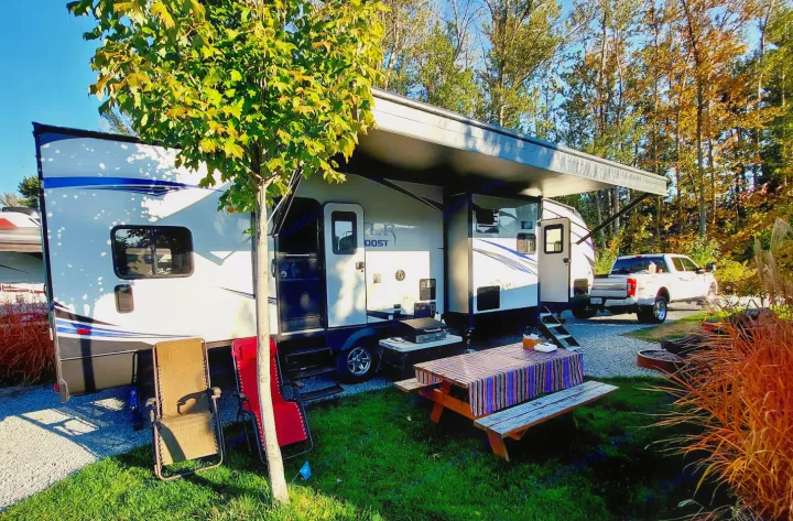 Spacious RV rental campsite with a white camper, extended awning, picnic table, and chairs. Truck in background.. Forest River XLR Boost Toy Hauler 2018