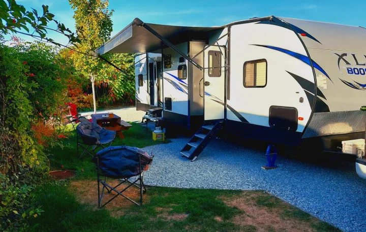 Spacious RV rental parked at a tranquil campsite, with a picnic table and comfy chairs set on the grass.. Forest River XLR Boost Toy Hauler 2018