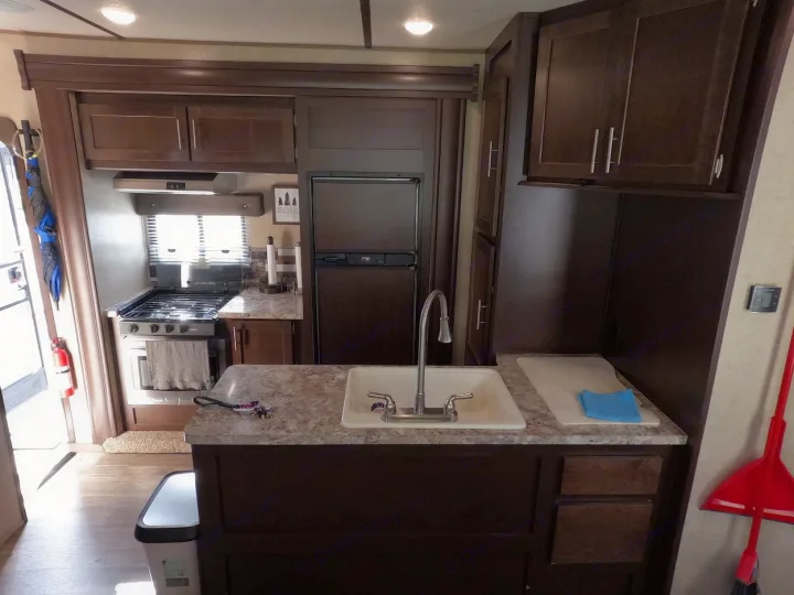 RV rental kitchen interior featuring stove, sink, refrigerator, and ample dark wood cabinetry. A cozy and functional space.. Forest River XLR Boost Toy Hauler 2018