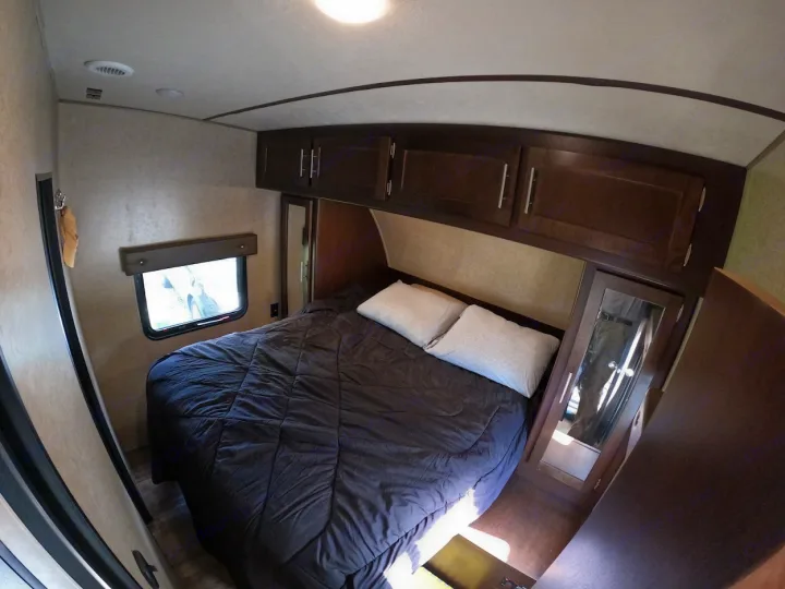 Cozy RV rental bedroom with a comfy bed, overhead cabinets, and window. Ideal for compact living.. Forest River XLR Boost Toy Hauler 2018