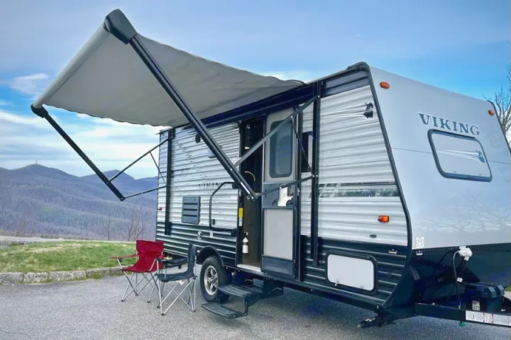 A gray Viking travel trailer (RV) with its awning extended and chairs set up. This RV rental offers peaceful mountain views.. Forest River Viking 2020