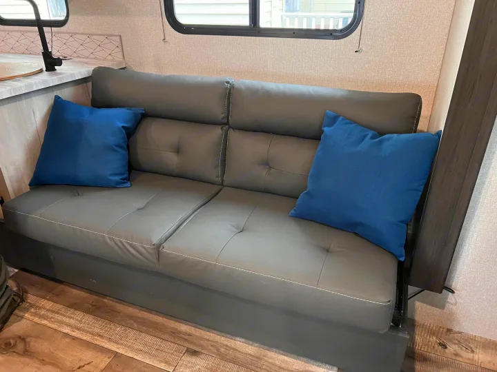 Cozy RV rental living space featuring a modern gray sofa with blue pillows, a kitchen counter, and windows.. Escape e231bh 2022
