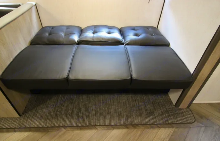 RV rental interior featuring a versatile black sofa bed with tufted back cushions and a gray rug.. Heartland RVs Prowler 2022