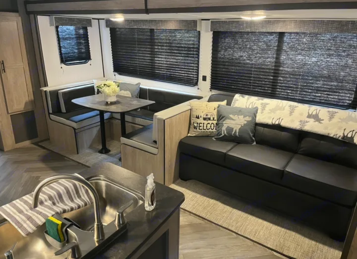 Stylish rv rental interior showing a comfortable dinette, black sofa with pillows, and a kitchen sink area.. Heartland RVs Prowler 2022