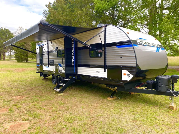 Spacious RV rental, a sleek gray & white travel trailer with an extended awning, parked in a grassy field. Great for camping trips.. Heartland Pioneer BH270 2023