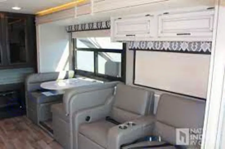 RV rental interior with a light wood floor, showcasing a dinette, two recliners, and bright overhead cabinets.. Jayco Precept 2020