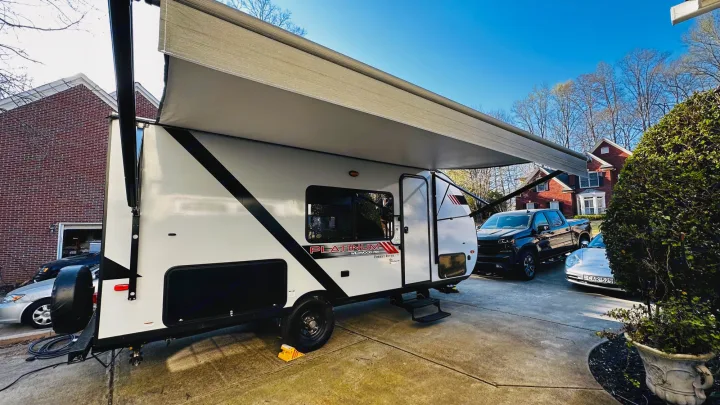 Spacious travel trailer with extended awning parked on a driveway next to a pickup truck. Ideal for your next rv rental!. Forest River Wildwood 2021