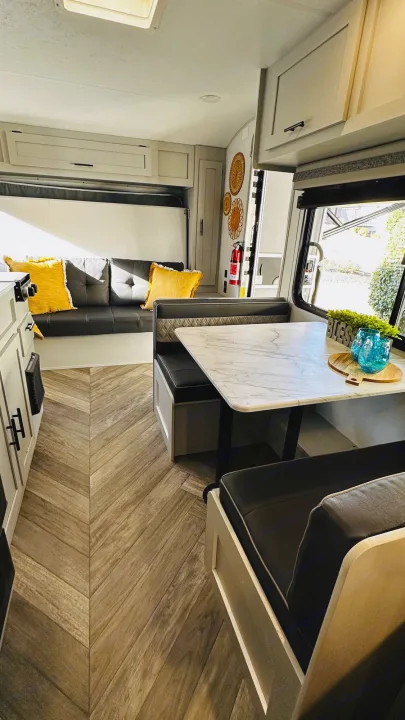 This inviting RV rental interior features a modern dinette, sofa with yellow pillows, and chic herringbone flooring.. Forest River Wildwood 2021
