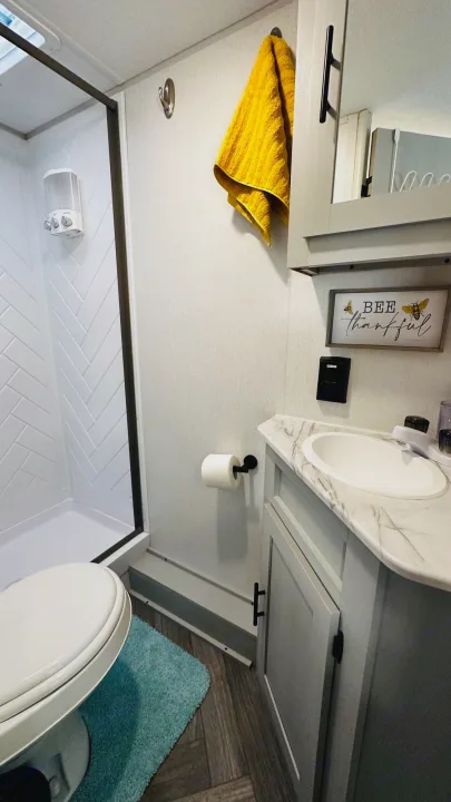 Comfortable RV rental bathroom featuring a shower, toilet, and sink with modern vanity and decor.. Forest River Wildwood 2021