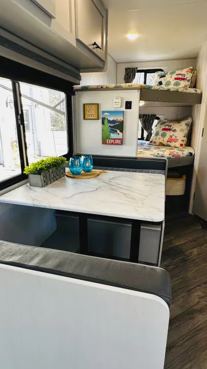 Bright RV rental interior featuring a dinette table with marble-look top, bench seating, and cozy bunk beds. Perfect for family adventures.. Forest River Wildwood 2021