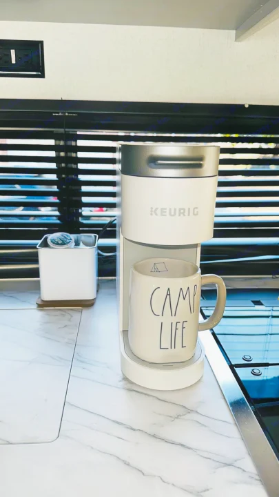 RV rental morning: A white Keurig coffee maker, "CAMP LIFE" mug, and K-cups on a sleek marble countertop.. Forest River Wildwood 2021