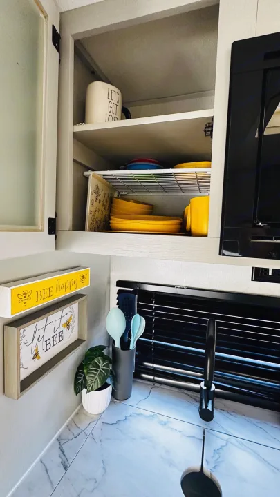 RV rental kitchen: organized cabinets with colorful dishes, bee decor, sink, and plant. A compact, functional space.. Forest River Wildwood 2021