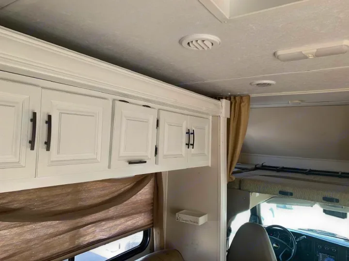 RV rental interior: White overhead cabinets, a cozy bunk over the cab, and driver's area for comfortable travel.. Forest River Sunseeker 2015