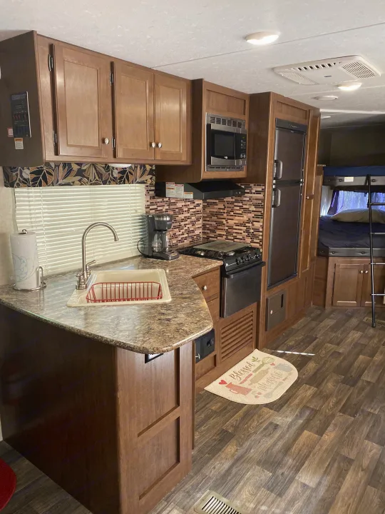 Inside an RV rental: a compact kitchen with a sink, microwave, stove, and a view of bunk beds, featuring wood-look flooring.. Keystone RV Hideout 2016