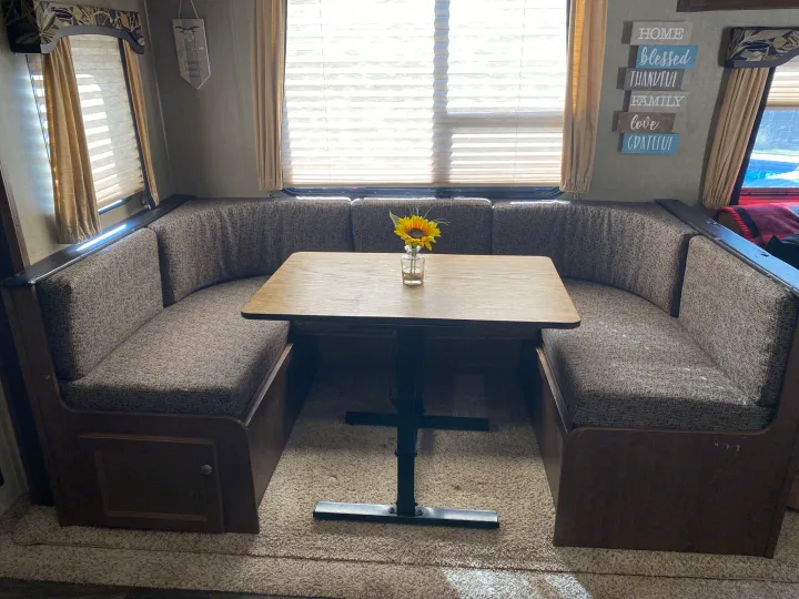 Comfortable RV rental dinette with U-shaped seating, wooden table, and sunflower vase, perfect for meals.. Keystone RV Hideout 2016