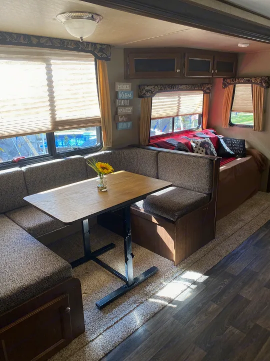 Inside a cozy RV rental, featuring a U-shaped dining booth, table, and bed area with homey decor and bright windows.. Keystone RV Hideout 2016