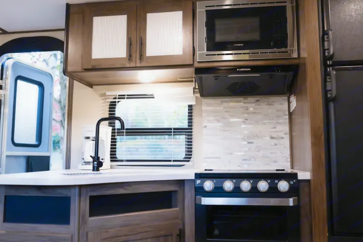 Functional RV rental kitchen showcasing a sleek sink, Furrion microwave & stove, and ample storage for trips.. Avenger ATI 2020