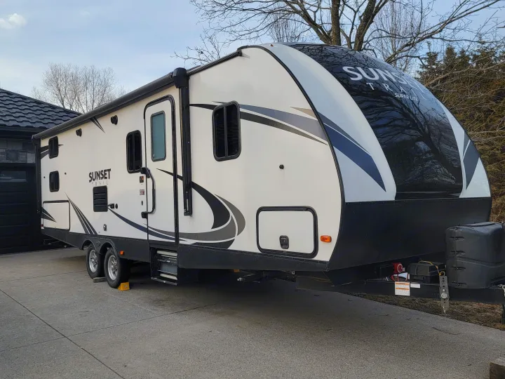 White & black Sunset Trail travel trailer, great for an rv rental. Parked on concrete driveway, ready for adventure.. Crossroads RV Sunset Trail Super Lite 2019