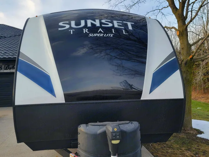 This RV rental features a white, black, and blue Sunset Trail Super Lite camper with a visible front propane tank.. Crossroads RV Sunset Trail Super Lite 2019