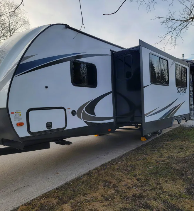 White RV rental, a Sunset Trail travel trailer with its slide-out extended, parked on a concrete pad.. Crossroads RV Sunset Trail Super Lite 2019