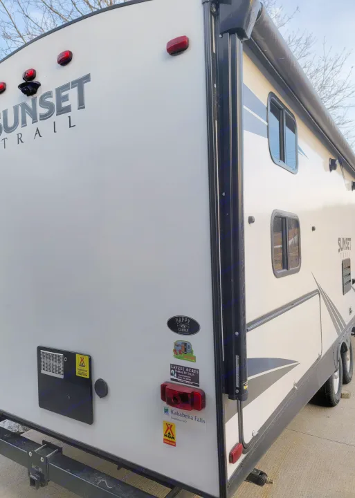 Rear view of a white "Sunset Trail" travel trailer, adorned with camping decals. Ideal for your next rv rental.. Crossroads RV Sunset Trail Super Lite 2019