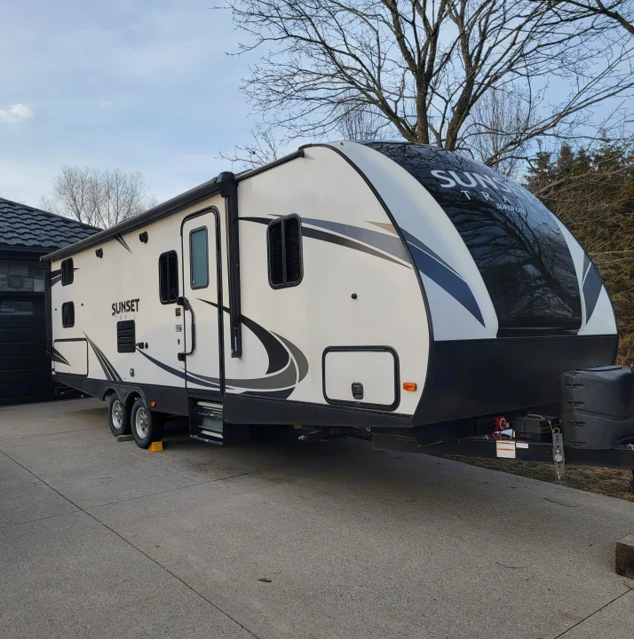 Sleek white Sunset Trail travel trailer RV parked on a concrete driveway. Explore the open road with this RV rental.. Crossroads RV Sunset Trail Super Lite 2019