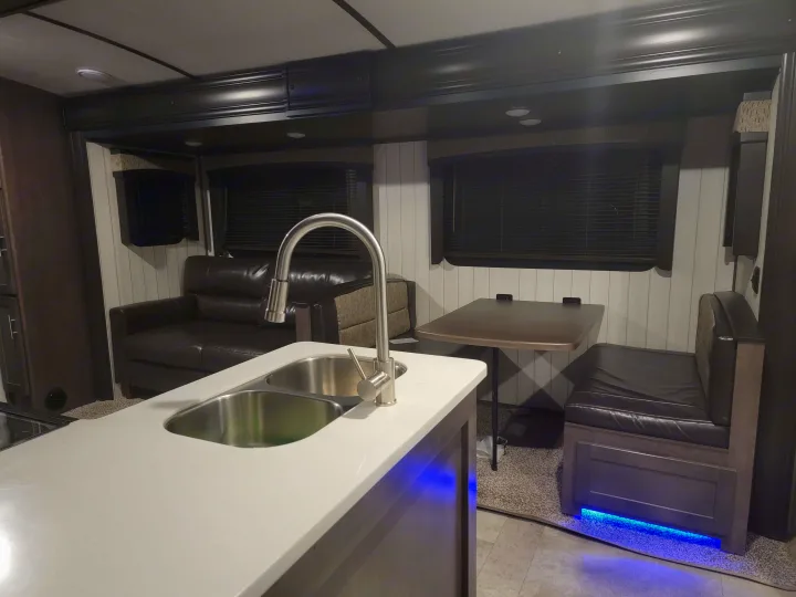 This RV rental interior features a kitchen with a sink, a comfortable sofa, and a dinette, all lit by blue LEDs.. Crossroads RV Sunset Trail Super Lite 2019
