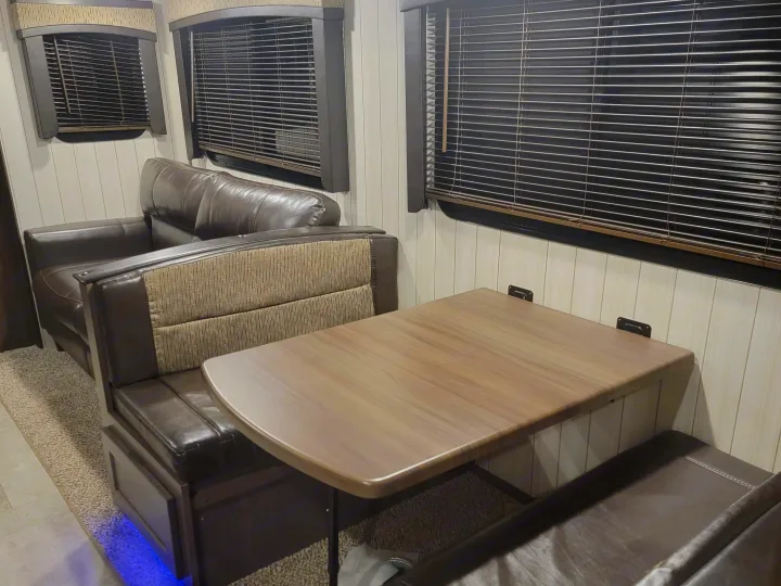 RV rental interior featuring a brown sofa, a dinette with a light wood table and benches, and windows with blinds.. Crossroads RV Sunset Trail Super Lite 2019
