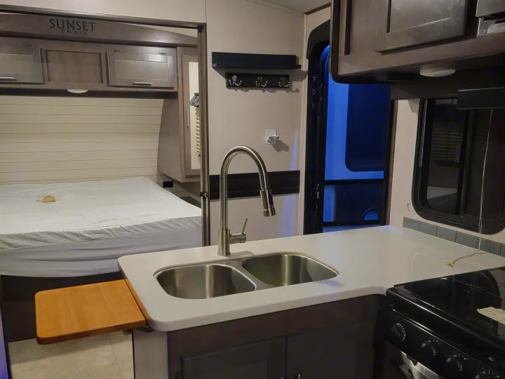 Sunset Trail RV rental interior featuring a practical kitchen with sink & counters, and a cozy bedroom with a bed.. Crossroads RV Sunset Trail Super Lite 2019