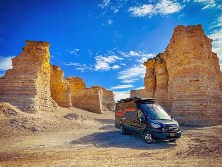 An RV rental van parked among the unique Niobrara Chalk rock formations under a bright blue sky.. Vandoit DO 2019