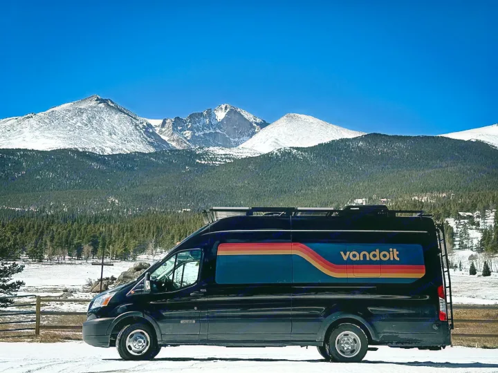 Black Vandoit RV rental van parked on snowy ground, with majestic snow-capped mountains and blue sky.. Vandoit DO 2019