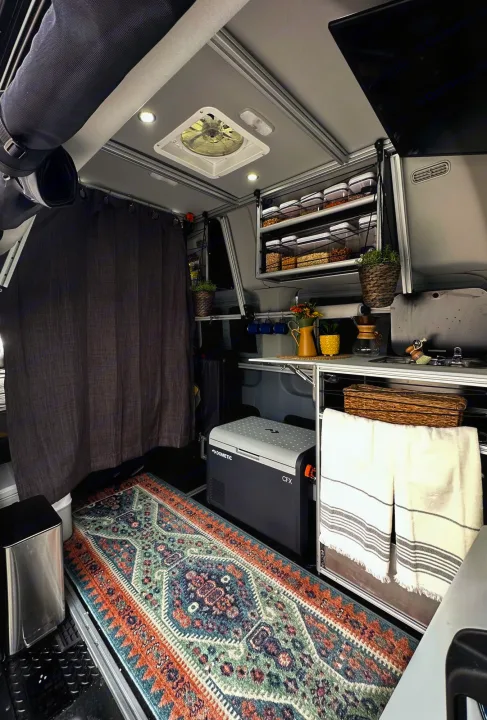 Cozy RV rental interior: compact kitchen area, Dometic fridge, organized overhead food storage, and a vibrant patterned rug.. Vandoit DO 2019