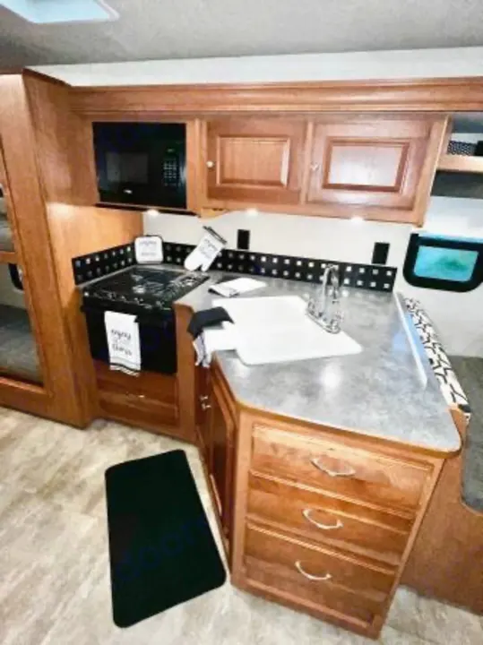 Spacious RV rental kitchen featuring a black microwave and stove, sink, wooden cabinets, and light countertops, perfect for your journey.. Winnebago Sunstar 2016