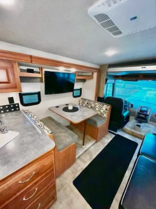 This rv rental interior features a kitchen counter, dining booth with TV, and a living area, all within a modern motorhome.. Winnebago Sunstar 2016