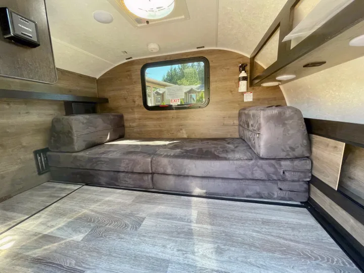 Inside a comfy RV rental: modular bed, wood-look interior, window, thermostat, and fire extinguisher for safe travel.. Braxton Creek Bushwhacker 2021