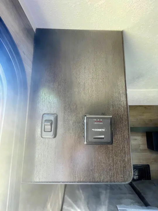 RV rental interior: A Dometic thermostat and a light switch are mounted on a wood-grain wall.. Braxton Creek Bushwhacker 2021
