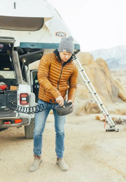 RV rental adventure: Man cooks by Jeep with rooftop tent & water system in rocky desert.. Jeep Gladiator 2022