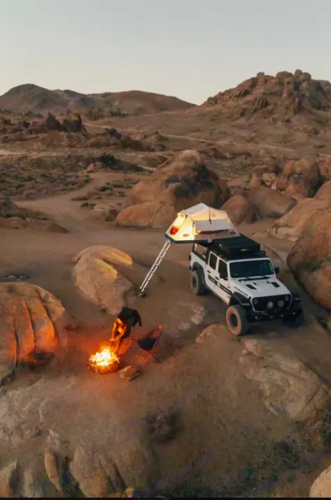 White Jeep Gladiator with rooftop tent and campfire in rocky desert. This ultimate adventure RV rental offers freedom for overlanding.. Jeep Gladiator 2022