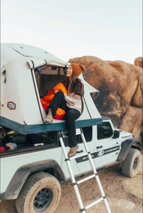 Woman in a rooftop tent on a white Jeep Gladiator RV rental. Enjoy overland camping and outdoor adventure.. Jeep Gladiator 2022