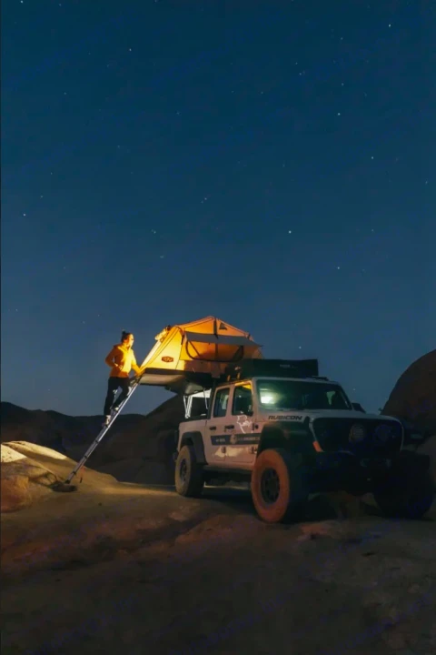 Starry night overlanding with an rv rental. Person on ladder accesses a lit roof-top tent on a white Jeep. Rugged outdoor adventure.. Jeep Gladiator 2022