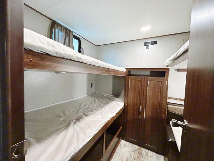 Inside this RV rental, find comfortable bunk beds with white linens, integrated storage, and a compact wardrobe, designed for cozy travel.. Zinger ZR29OKB 2018