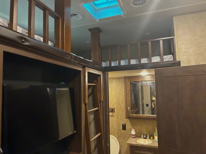 This RV rental shows a lofted bunk bed area with a TV, ladder, and compact bathroom, highlighting efficient interior space.. Forest River Sandpiper 2018