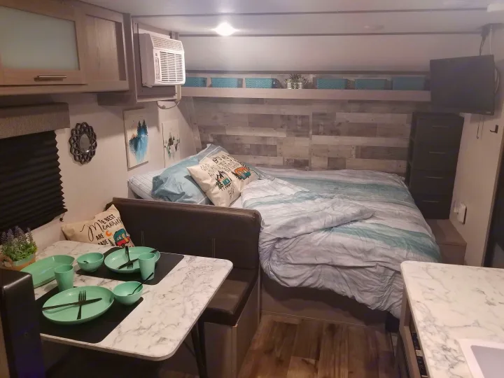 Experience comfort in this RV rental! Features include a cozy bed, a dining area with mint green place settings, and ample storage.. Coleman Lantern 17B 2023