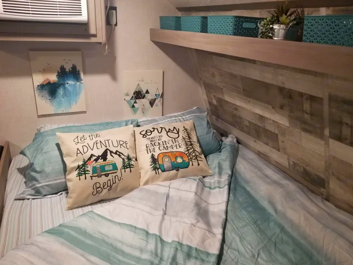 Inside a stylish rv rental: a cozy bed with camping-themed pillows, wood paneling, & teal storage. Ready for adventure!. Coleman Lantern 17B 2023