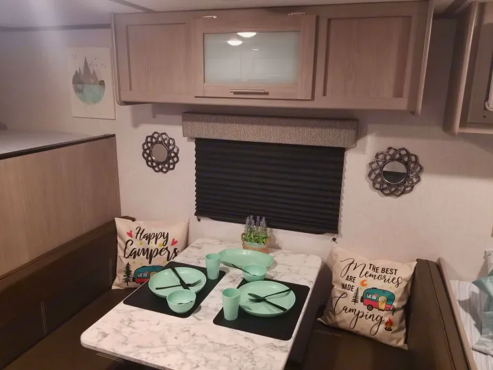Cozy RV rental interior showcasing a modern dining dinette with camping-themed pillows, upper cabinets, and a bunk bed.. Coleman Lantern 17B 2023